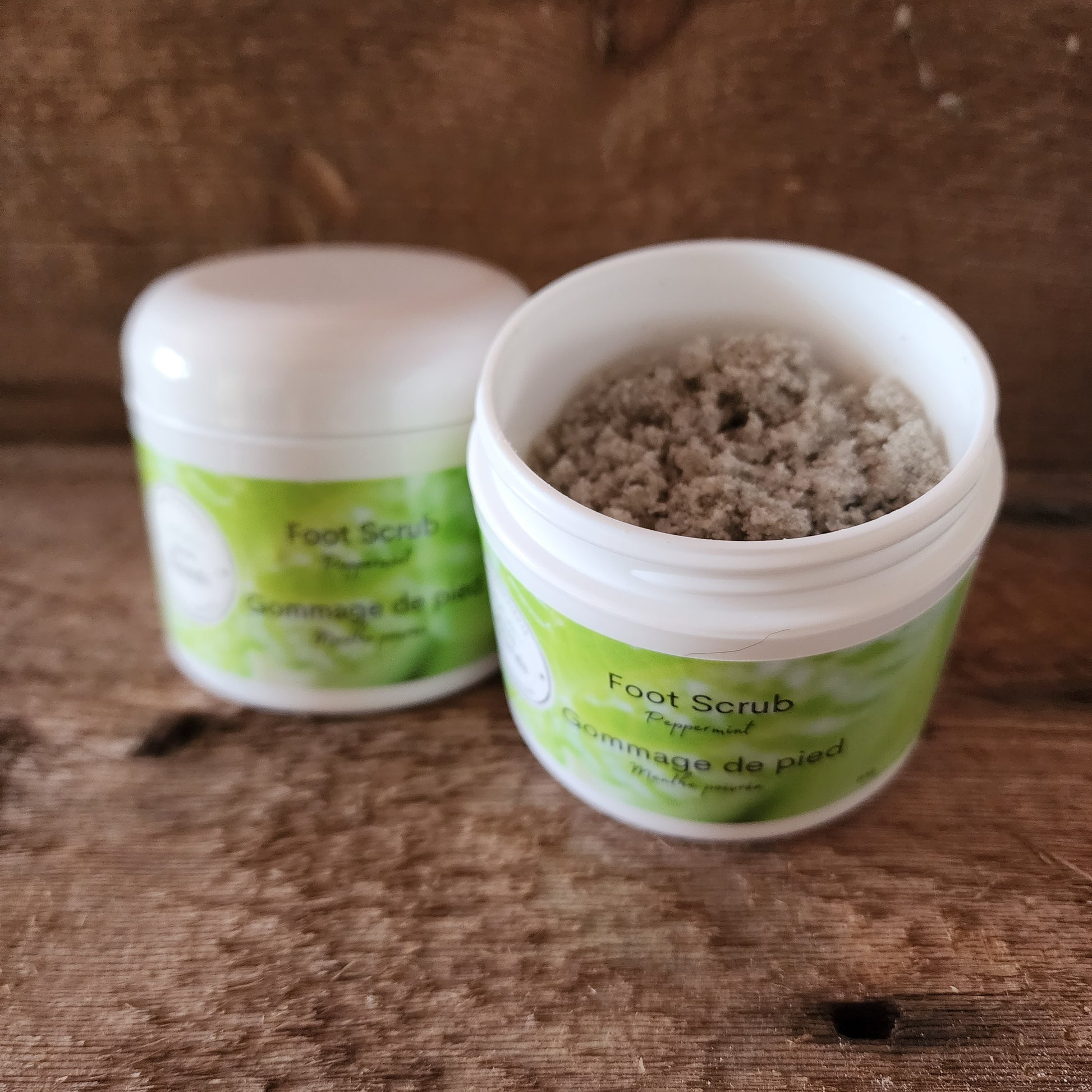 An open jar of foot scrub with a solid content that resembles a coarse grain texture, placed on a wooden surface.