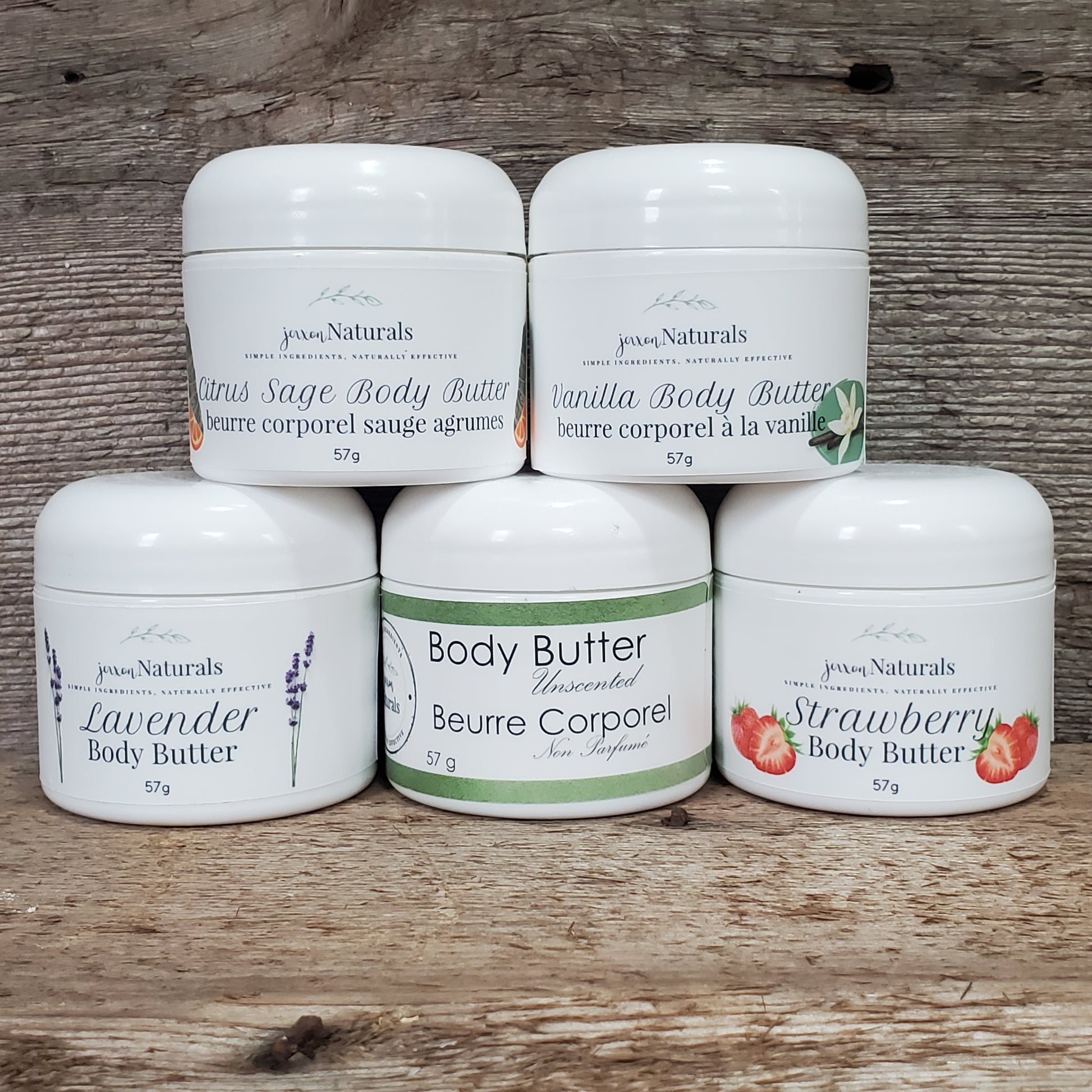 Jars of body butter in various scent options including unscented, lavender, and strawberry, arranged on a wooden surface.