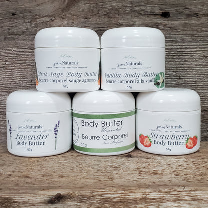 Jars of body butter in various scent options including unscented, lavender, and strawberry, arranged on a wooden surface.