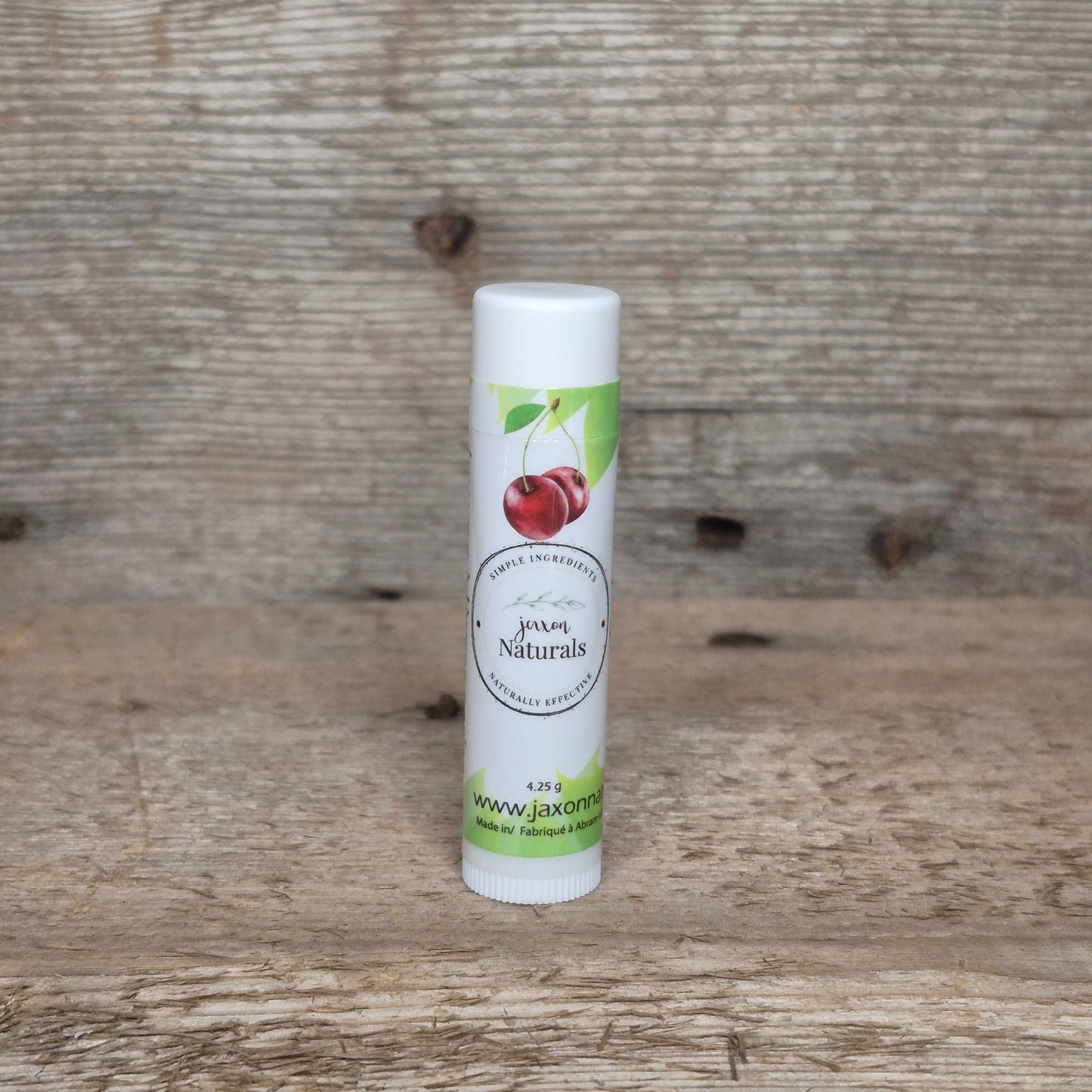 Jaxon Naturals Cherry Lip Balm in a recyclable tube, handcrafted with natural ingredients and displayed on rustic barn wood.