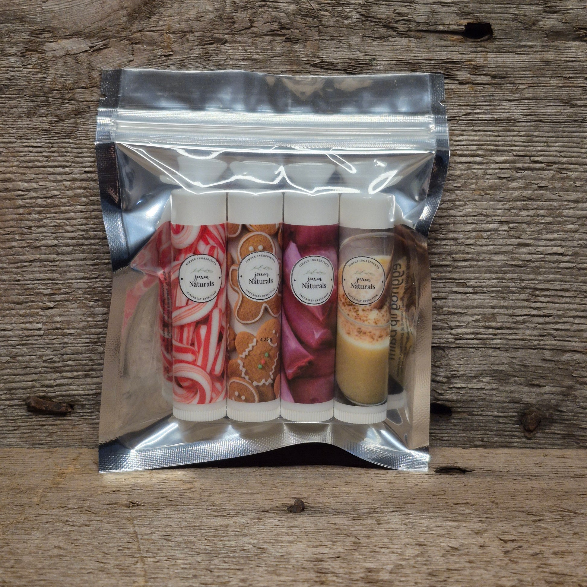 Jaxon Naturals Christmas Lip Balm Collection featuring four handcrafted holiday lip balms displayed on rustic barn board.