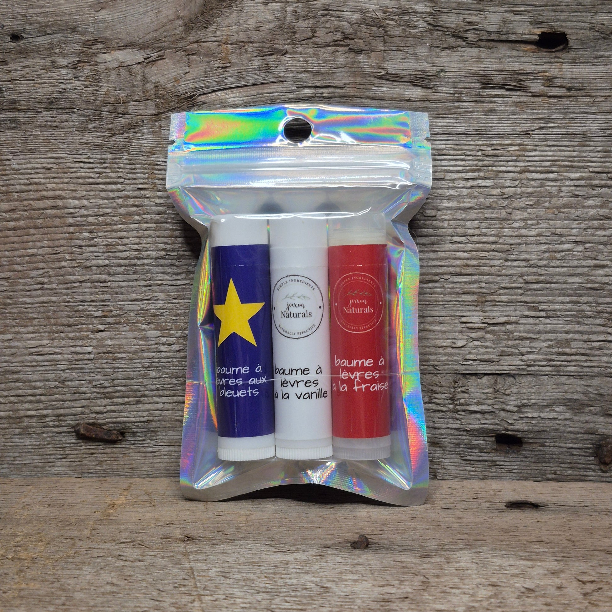 Jaxon Naturals Acadian lip balm collection with three handcrafted Acadian-inspired lip balms displayed on rustic barn board.