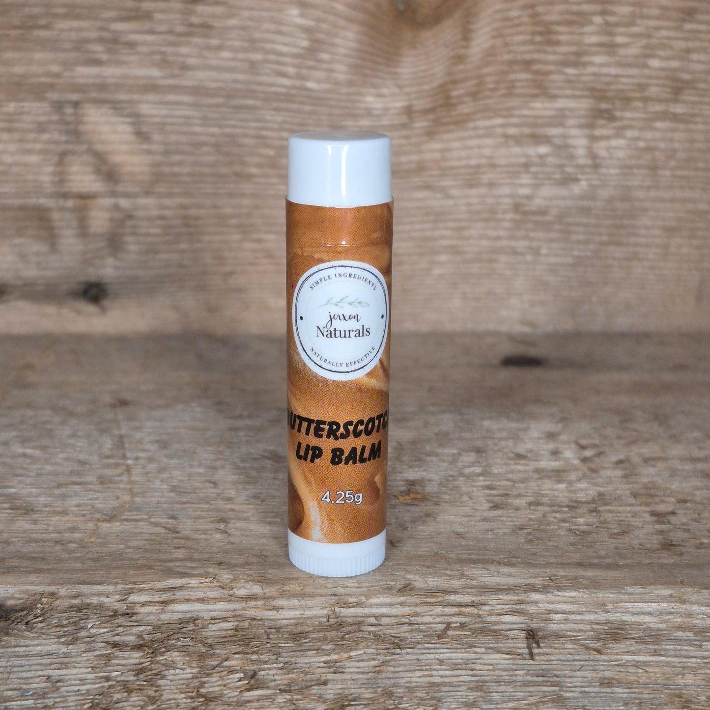 Jaxon Naturals limited edition butterscotch lip balm displayed on rustic barn board.
