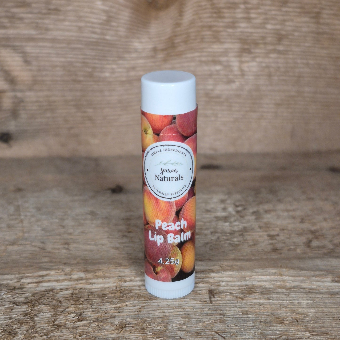 Jaxon Naturals limited edition peach lip balm displayed on rustic barn board.