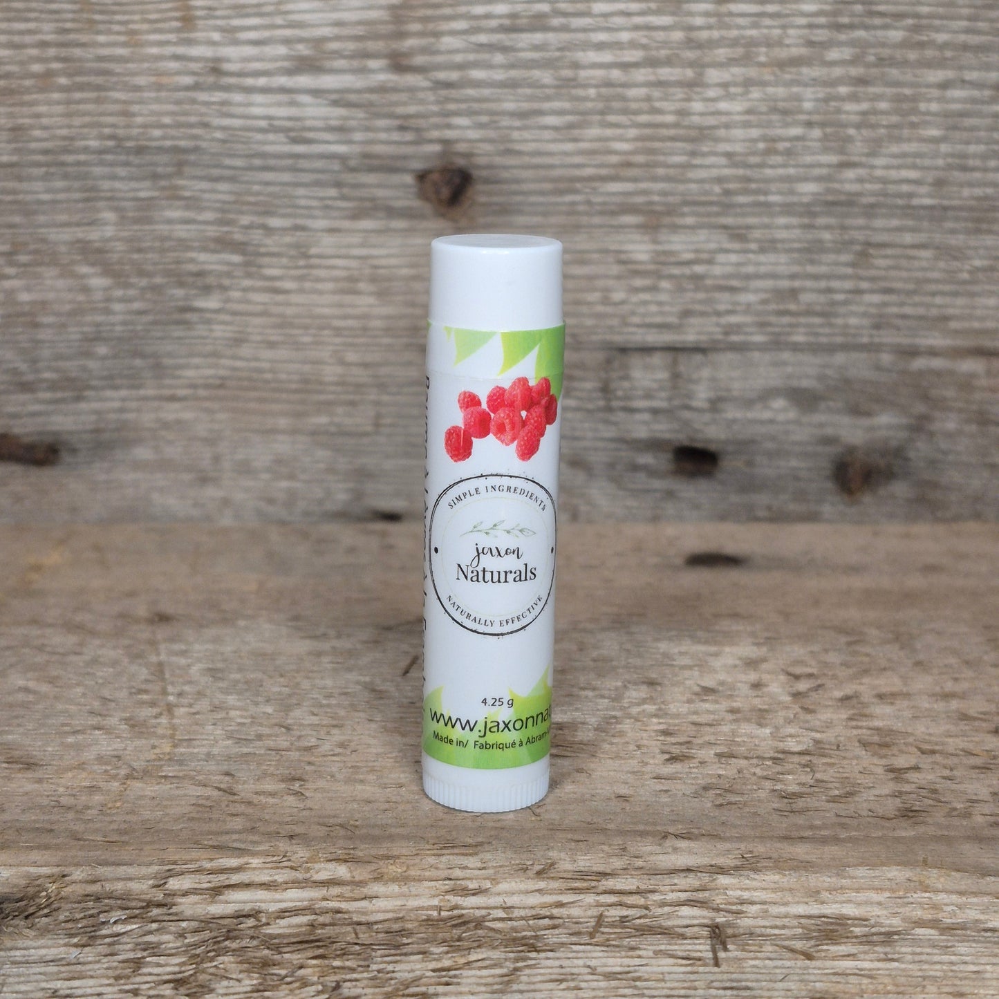 Jaxon Naturals Raspberry Lip Balm in a recyclable tube, handcrafted with natural ingredients and displayed on rustic barn wood.
