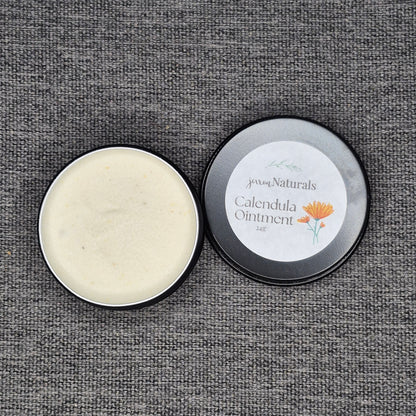 Open tin of Calendula Ointment with visible cream inside on a textured gray background