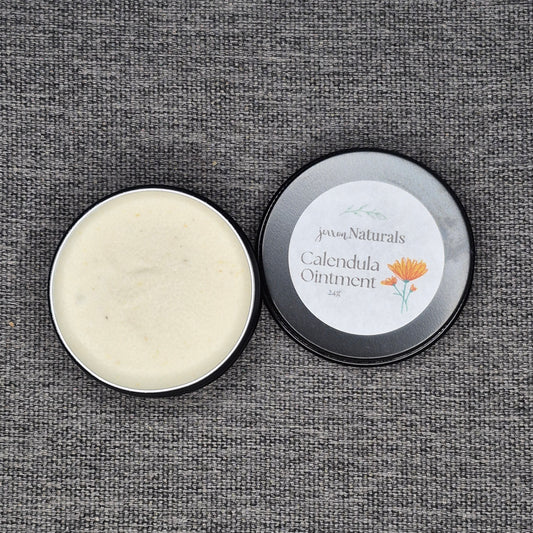 Open tin of Calendula Ointment with visible cream inside on a textured gray background