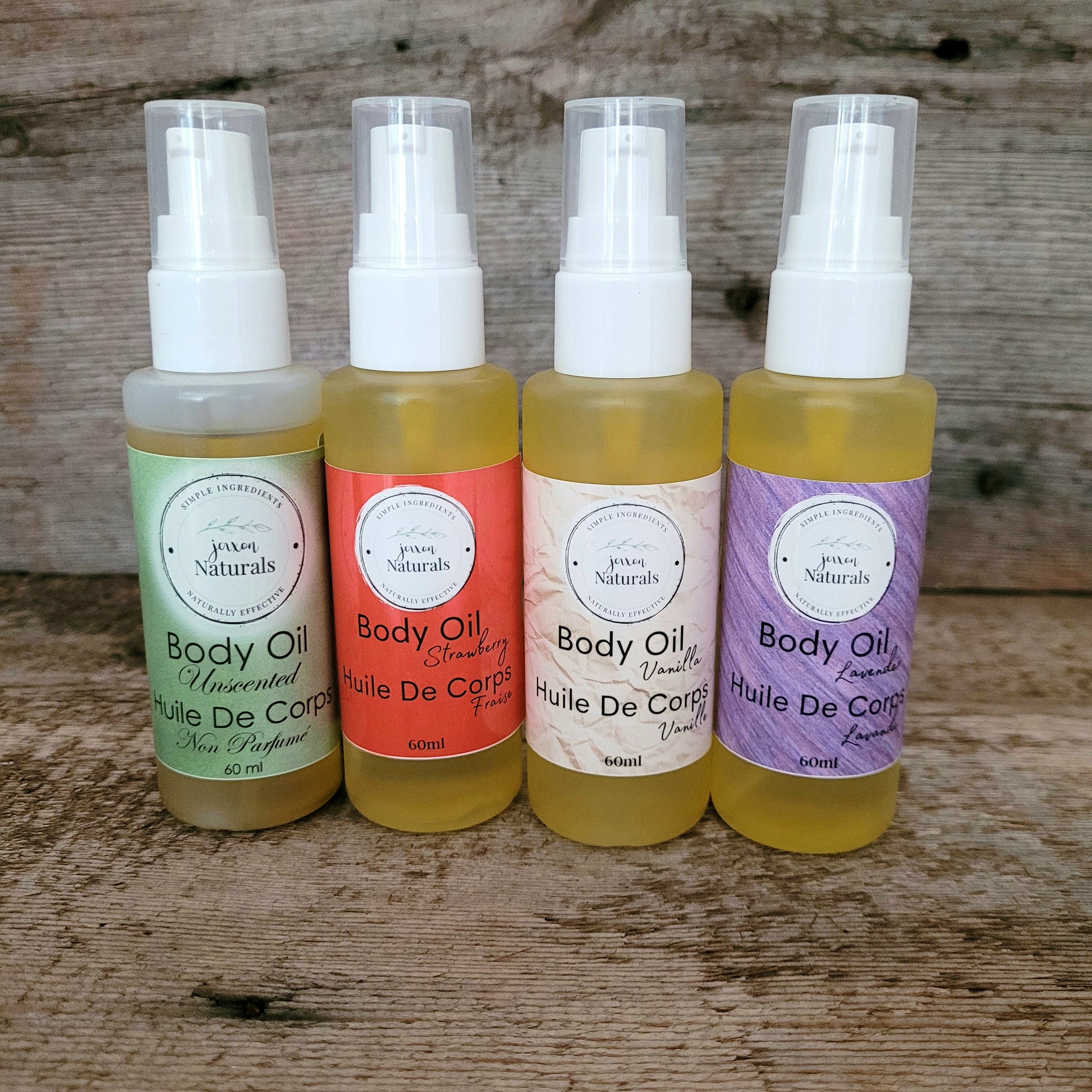 Four bottles of body oil with different colored labels, arranged side by side on a wooden surface.